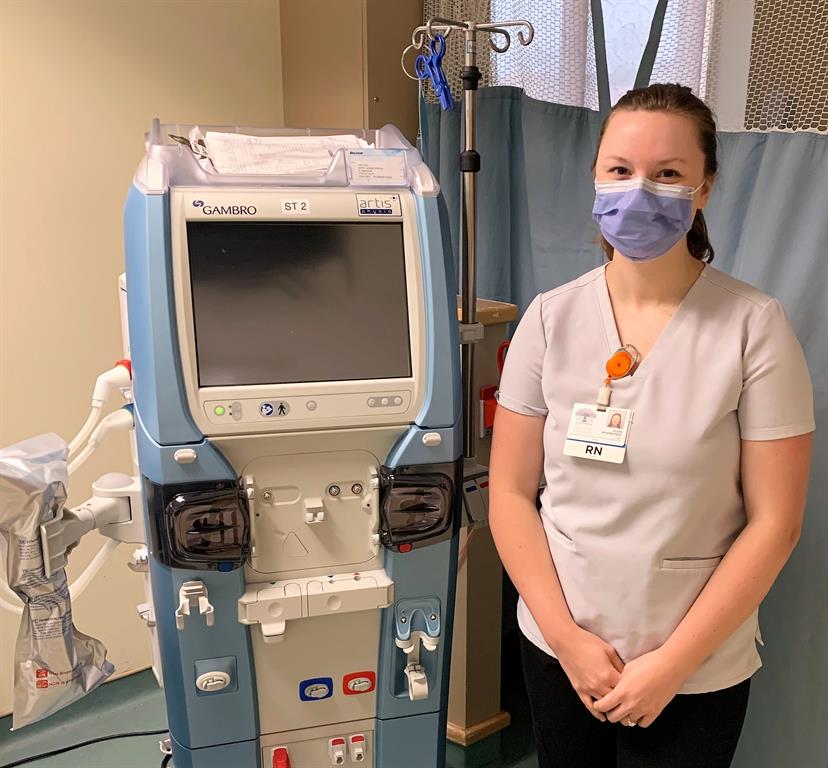 Alex, RN stands beside a dialysis machine